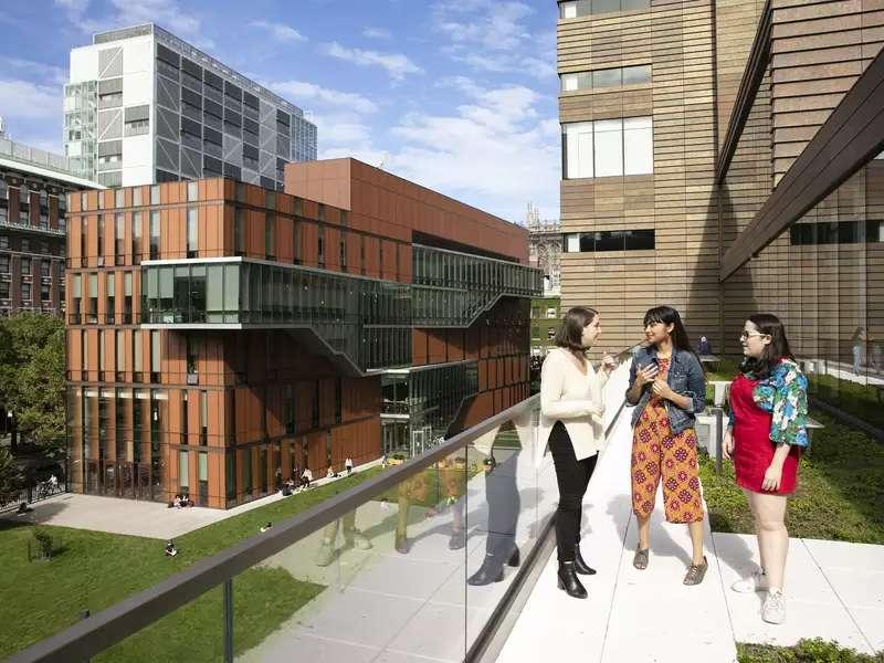 3 students stand on a balcony overlooking Barnard's campus